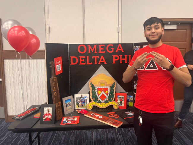 SMU Omega Delta Phi president Miguel Arroyo poses with his fraternity's hand symbol in front of their booth at the Multicultural Greek Council Open House.